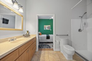 A bathroom with a sink, toilet, shower, and a bed in the adjacent room. - Banana Leaf Villa (Orlando)
