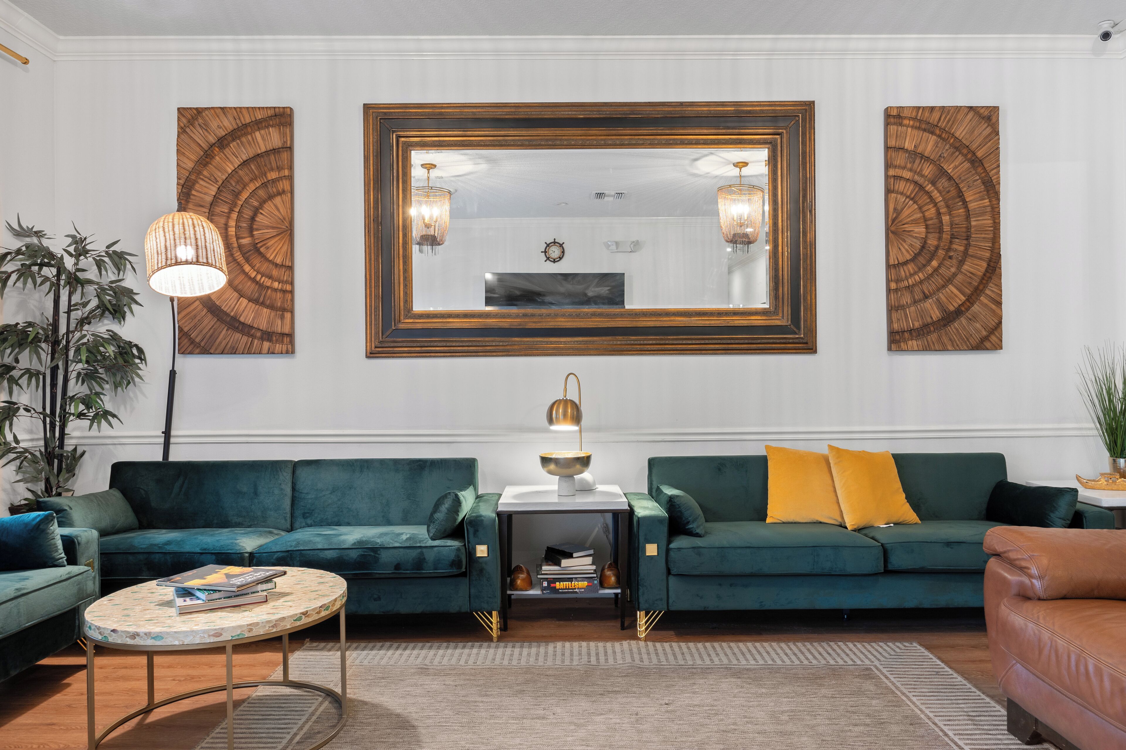 A living room with two green sofas, a round coffee table, a side table with a lamp, and a large mirror above the sofas.