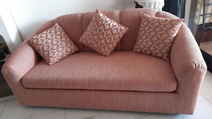 A pink sofa with patterned cushions in a room with white tiled flooring and a white wall.