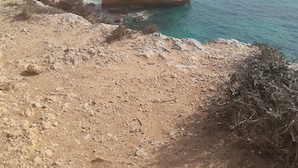 A coastal landscape with rocky cliffs, a sandy beach, and clear blue sea.