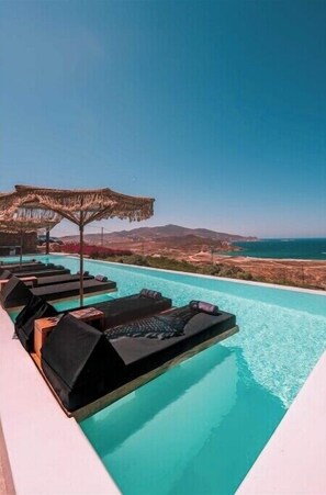 A poolside area with lounge chairs and a thatched umbrella, overlooking a coastal landscape.