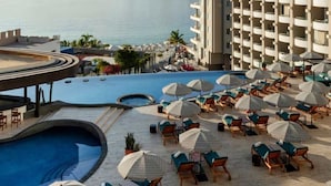 A resort pool area with multiple sun loungers and umbrellas, a large pool, and a view of the sea and mountains. - Corazón Tower - Infinity King Sunset View with Hot Tub (Cabo San Lucas)