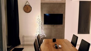 A modern dining area with a wooden table, black chairs, a flat-screen TV mounted on the wall, and a decorative light installation. - Welcome to Casa Beausite (Gap)