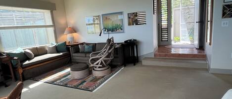 Una sala de estar con un sofá, una mesa de centro, una lámpara y una alfombra. Hay una puerta que da a un patio.