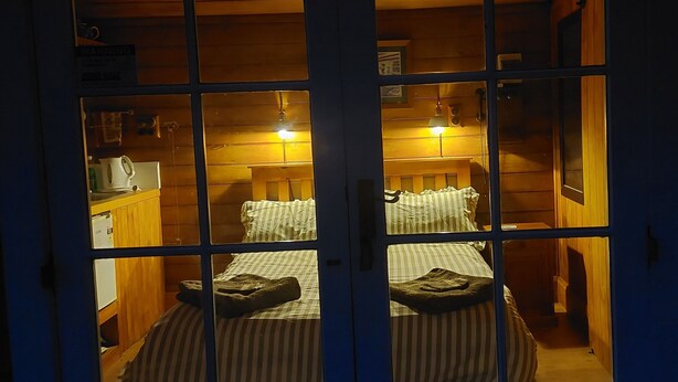 A room with a bed, a desk, and a chair. There is a window with a view of another room.