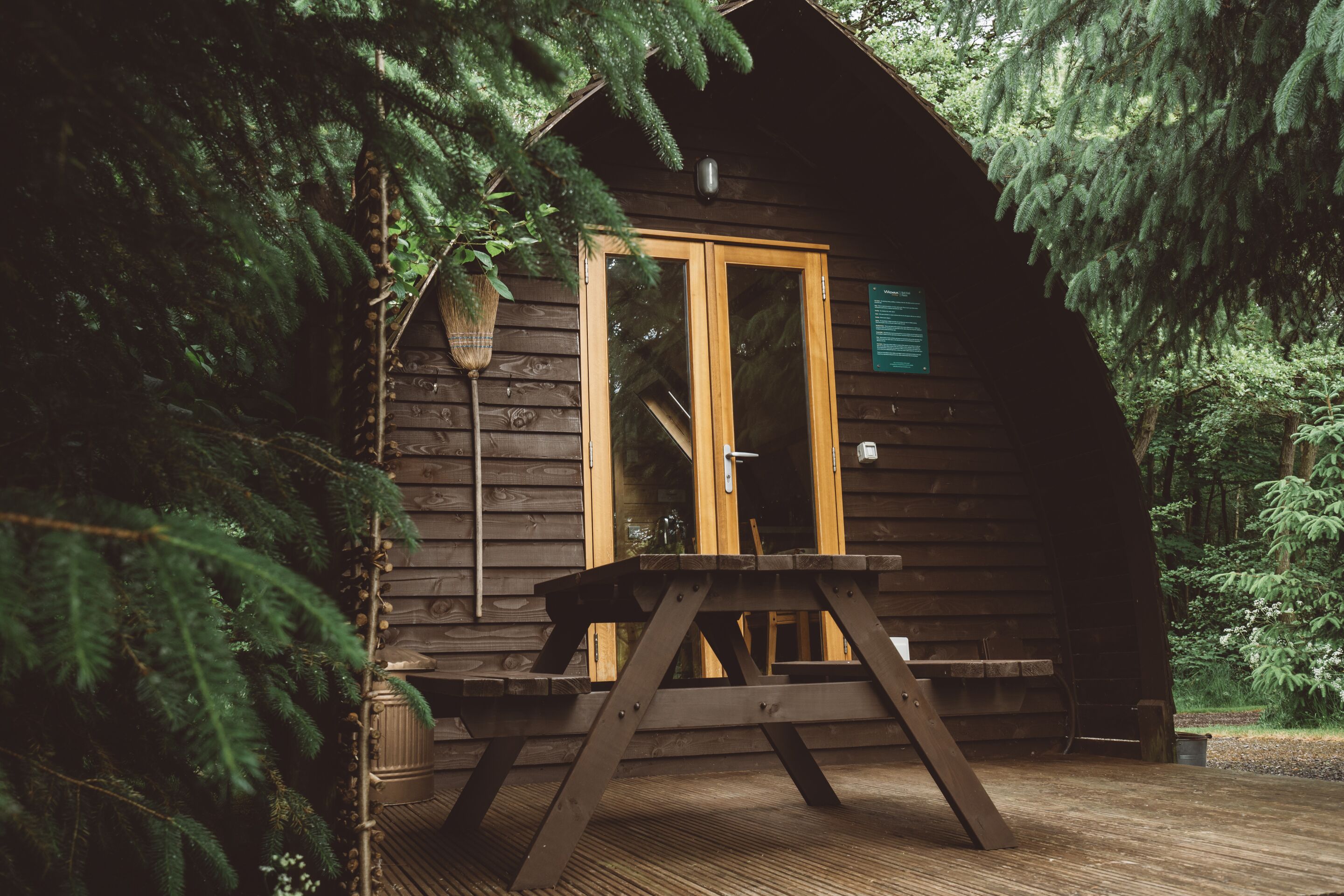 Una cabaña de madera con puerta de cristal, una mesa de picnic y un cartel en la puerta.