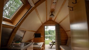 A cozy, wooden interior with a kitchen area, dining space, and a view of a pond. - Cosy Cabin in Idyllic Woodland Setting (Storwood)