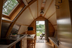 A cozy, wooden interior with a kitchen area, dining space, and a view of a pond. - Cosy Cabin in Idyllic Woodland Setting (Storwood)