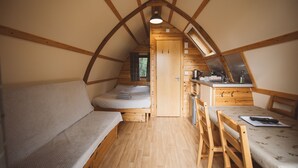 A cozy, compact room with a loft bed, a small kitchenette, and a dining area. - Cosy Cabin in Idyllic Woodland Setting (Storwood)