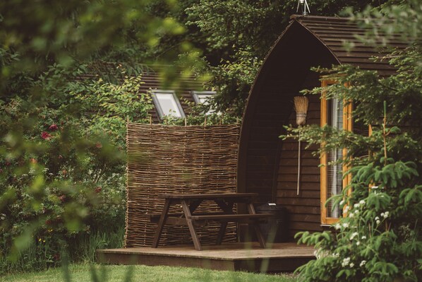 A rustic wooden cabin with a thatched roof, a wooden bench, and a picnic table. - Cosy Cabin in Idyllic Woodland Setting (Storwood)
