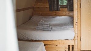 A wooden bunk bed with white bedding and a window with curtains. - Cosy Cabin in Idyllic Woodland Setting (Storwood)