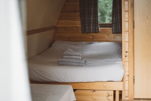Un lit superposé en bois, avec une literie blanche et une fenêtre agrémentée de rideaux.