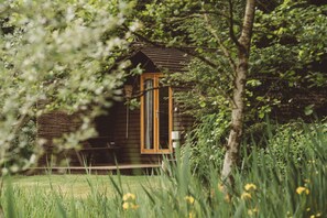 A rustic cabin surrounded by lush greenery and tall grass. - Wigwam Holidays Cabin with ensuite and kitchen (Storwood)