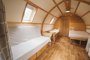 Ein gemütlicher, kompakter Raum mit Holzboden, einer Couch, einem Bett und einem kleinen Schreibtisch mit Stuhl.