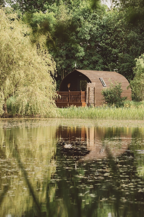 Een houten vakantiehuisje aan een meer, met een houten terras en een stenen muur.