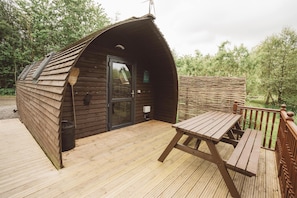 Een houten hut met een gebogen dak, een deur en een kleine tafel op een terras.