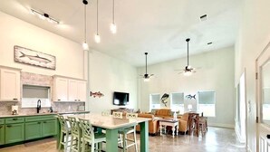 A spacious kitchen with green cabinets, a dining area with a large table, and a living room with a sofa and TV.