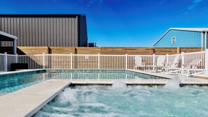 A swimming pool with a wooden deck and white chairs, surrounded by a white fence.