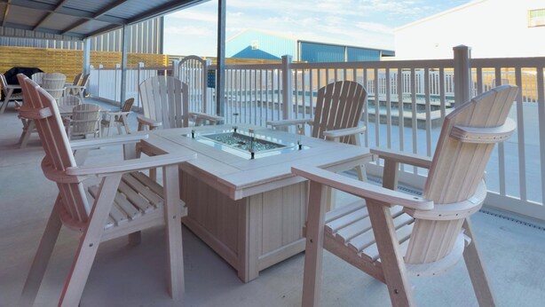 A covered outdoor seating area with a table and chairs, overlooking a building and a mountain.