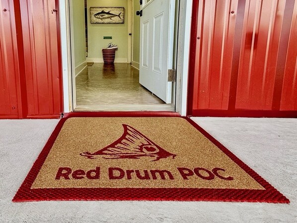 Un pasillo con alfombra roja que conduce a una puerta, un cuadro en la pared y un bote de basura al fondo.