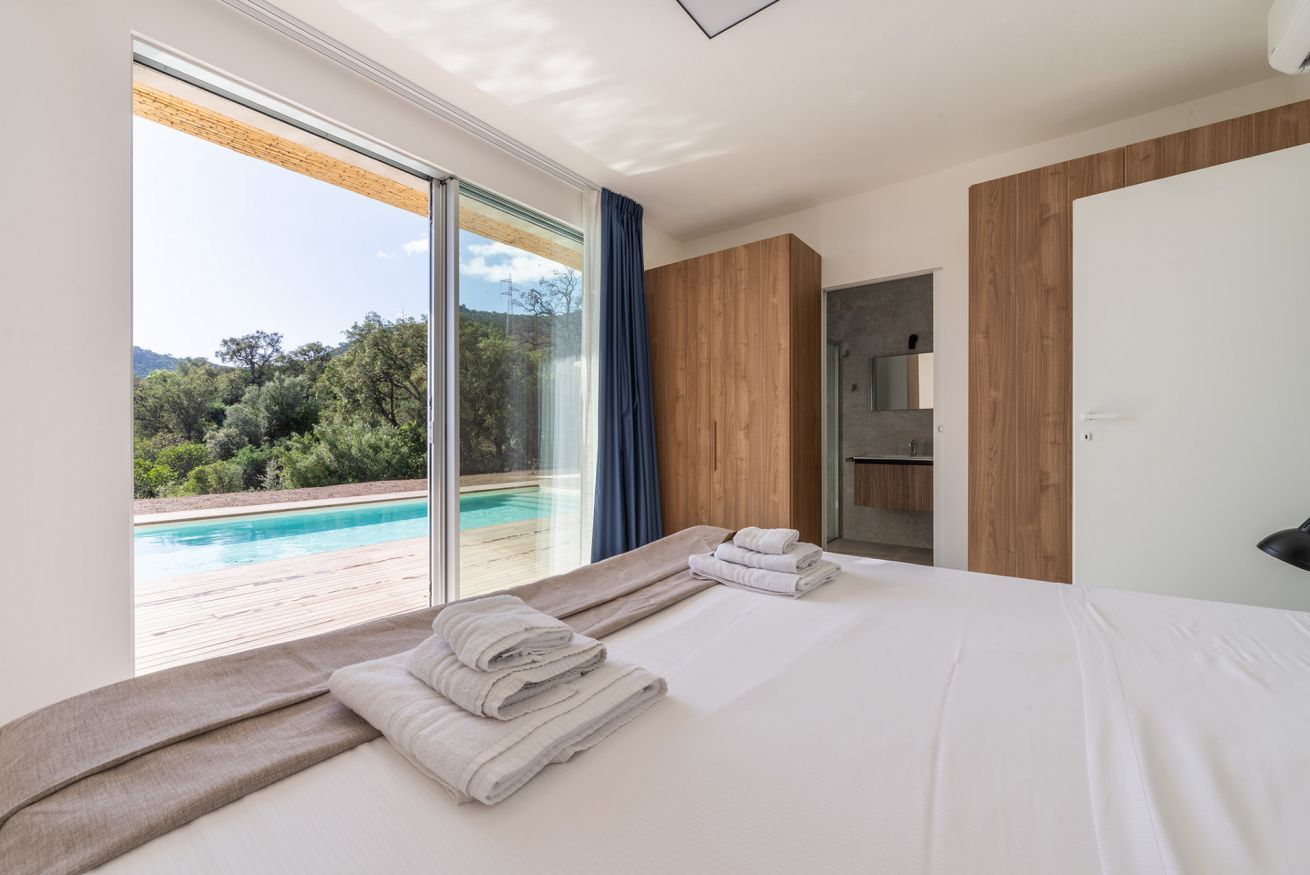 A bedroom with a large bed, a view of a swimming pool, and a wooden wall.