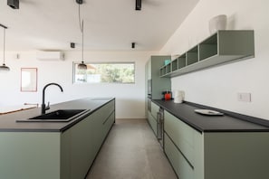 Une cuisine moderne dotée d’un îlot central, d’appareils électroménagers intégrés et d’une fenêtre laissant entrer la lumière naturelle.