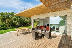 A modern outdoor deck with a dining area, seating, and a glass wall offering a view of the landscape. - Villa Gali – Luxury and Comfort in Is Molas, Pula (Is Molas)