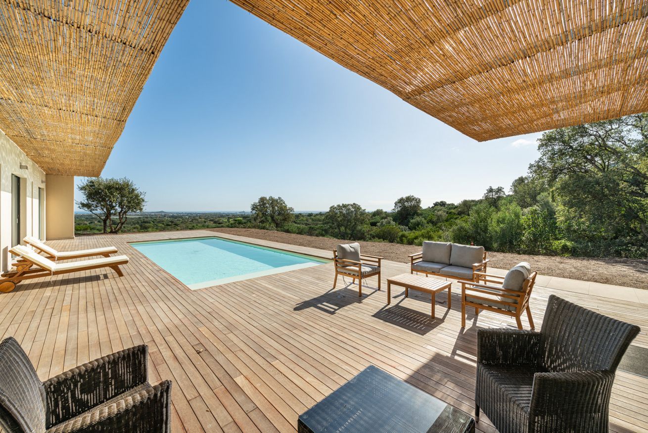 Une terrasse en bois avec une piscine, des chaises longues et du mobilier d’extérieur.