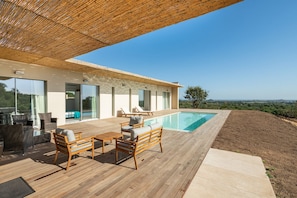 Un espace piscine extérieur moderne, doté d’une terrasse en bois, de chaises longues et offrant une vue dégagée sur le paysage.