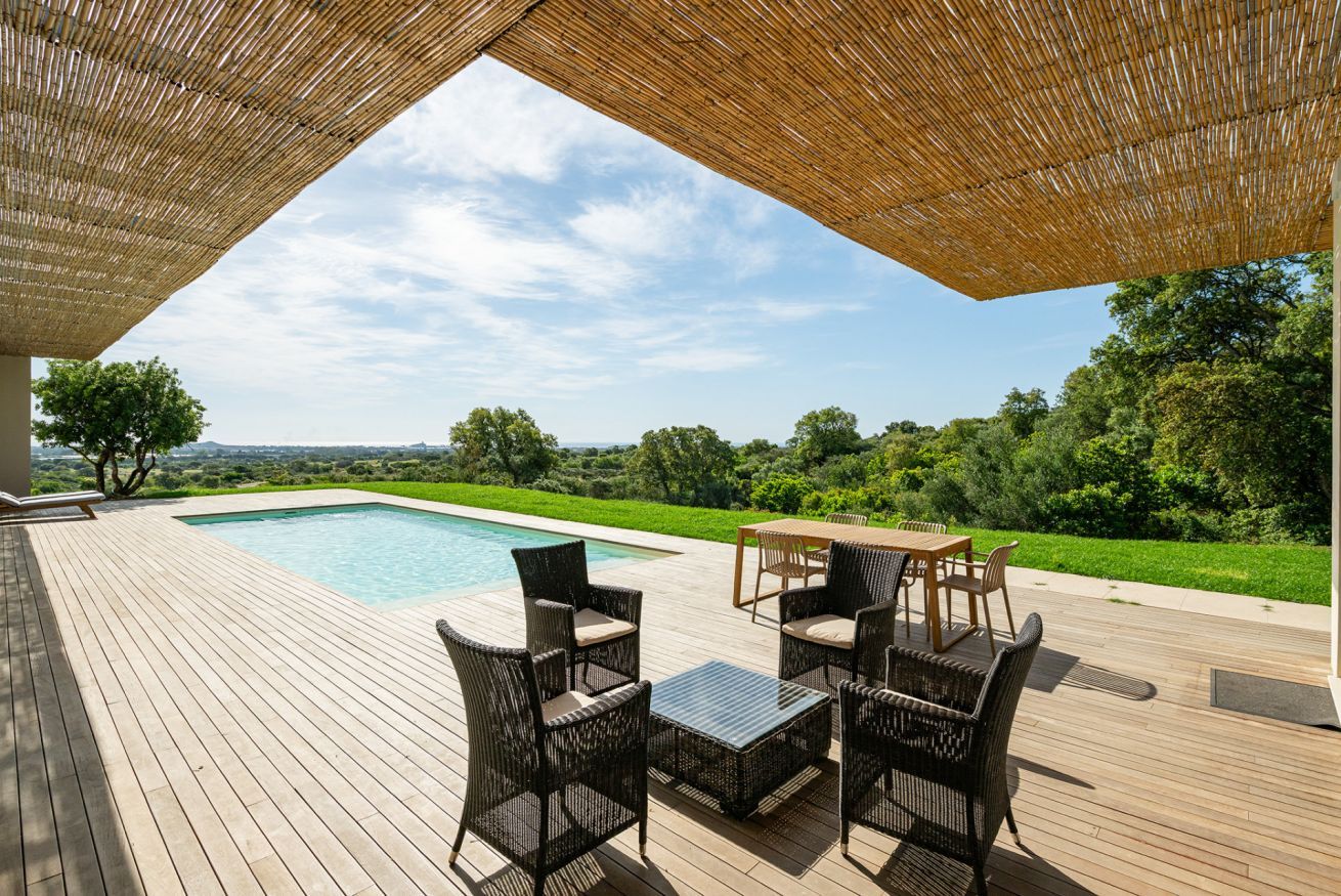 Una terrazza esterna con piscina, mobili in vimini e vista su un paesaggio verde.
