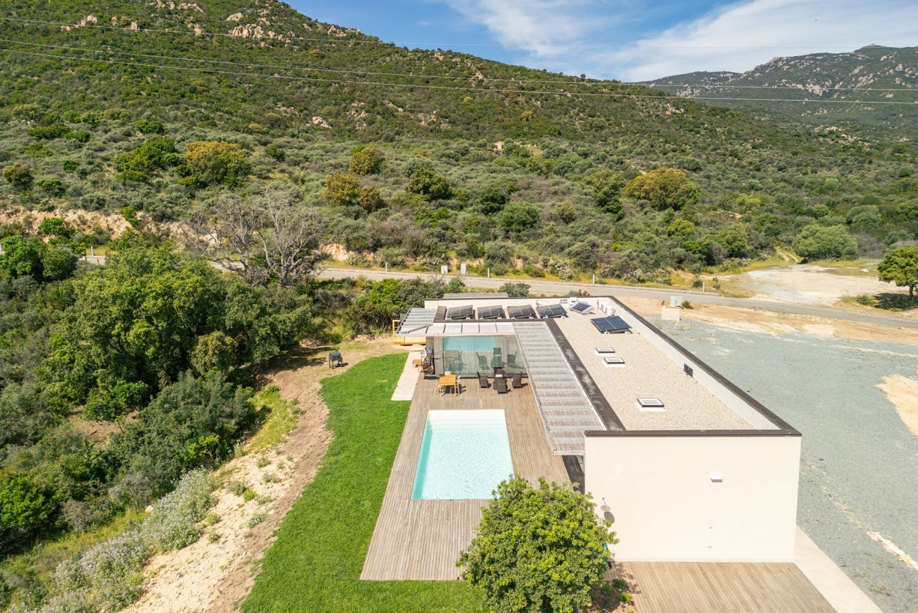 A modern building with a rooftop pool, surrounded by lush greenery and hills.