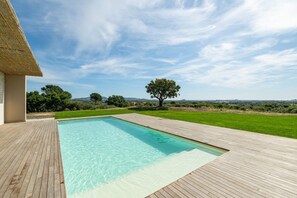 A swimming pool with a wooden deck, surrounded by a grassy lawn and trees, with a clear sky above. - Villa Valentina – Luxury and Comfort in Is Molas, Pula (Pula)
