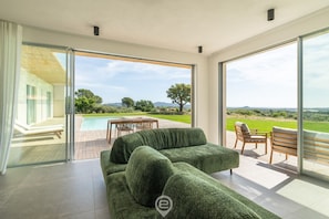 A modern living room with a green sofa, a dining area with wooden chairs, and a view of a swimming pool and landscape. - Villa Valentina (Pula)