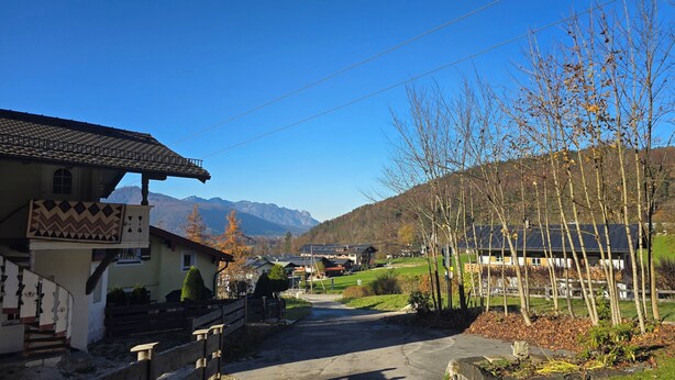Uma vila rural com edifícios tradicionais, céu claro e montanhas ao fundo.