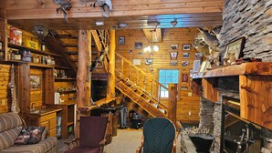 L’intérieur d’une cabane en rondins, avec un escalier en bois, une cheminée et divers trophées de chasse.