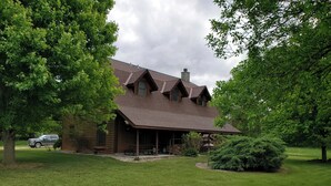 Un chalet rustique en rondins de bois, doté d’un porche abrité, entouré d’une végétation luxuriante et d’une pelouse bien entretenue.