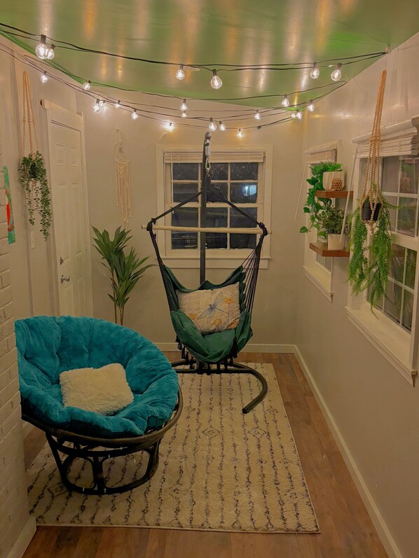 Une pièce chaleureuse avec un fauteuil turquoise, un fauteuil suspendu et des guirlandes lumineuses.
