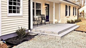 A single-story house with a covered porch, a small outdoor seating area, and a gravel driveway. - Updated 4-bedroom house with relaxing sunroom; minutes from downtown Raleigh. (Garner)