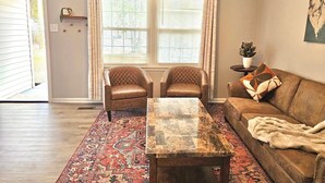 A living room with a wooden coffee table, two armchairs, a sofa, a patterned rug, and a ceiling fan. - Updated 4-bedroom house with relaxing sunroom; minutes from downtown Raleigh. (Garner)