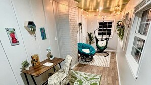 A narrow hallway with a wooden floor, a green patterned rug, a wooden table with a chair, and a hanging chair with a cushion. - Updated 4-bedroom house with relaxing sunroom; minutes from downtown Raleigh. (Garner)
