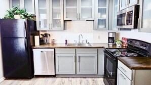 A modern kitchen with grey cabinets, a black refrigerator, a dishwasher, a sink, a stove, and a microwave. - Updated 4-bedroom house with relaxing sunroom; minutes from downtown Raleigh. (Garner)