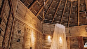 A room with a thatched roof, wooden walls, a bed with a canopy, and a green sofa. - Aldea Bamboo Village (San Francisco)