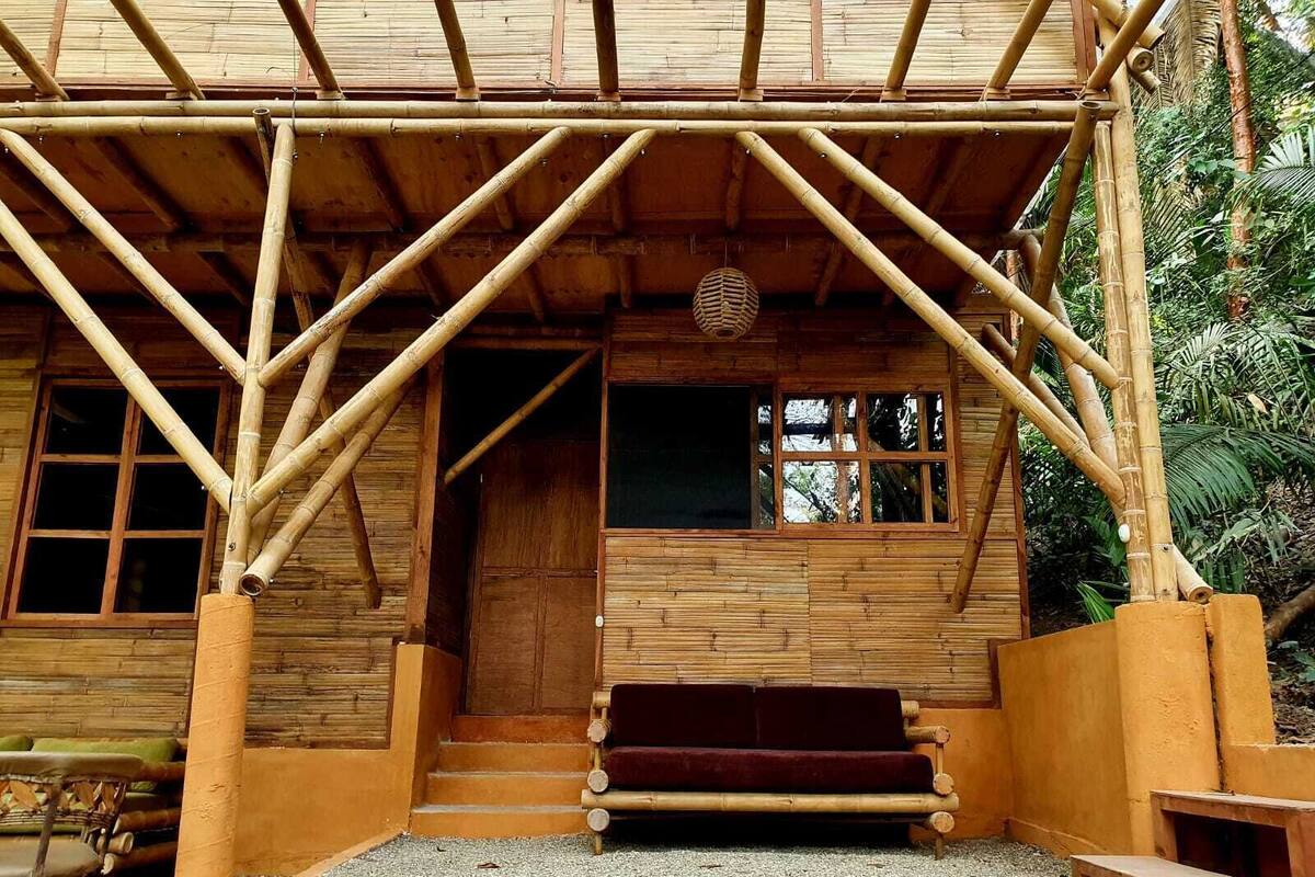 A bamboo structure with a wooden door and windows, a bench, and a small table.