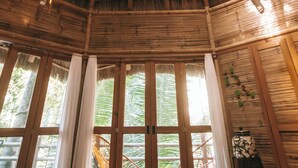 A room with a thatched roof, large windows, and a wooden floor. - Aldea Bamboo Village (San Francisco)