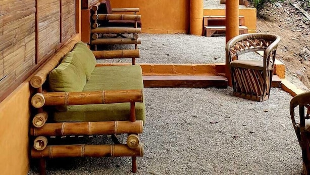 A bamboo-framed structure with a wooden exterior, a seating area with cushions, and a gravel ground. - Aldea Bamboo Village (San Francisco)