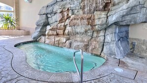 Een zwembad met een waterval, omringd door stenen muren en een betegelde vloer.