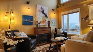 A cozy living room with a fireplace, comfortable seating, and artwork on the walls. - Pilley's Perch - Entire home in Pilley's Island, Canada. Beautiful Ocean View (Pilley's Island)