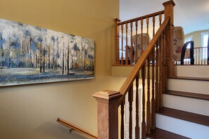 Eine Holztreppe mit Geländer, ein Baumgemälde an der Wand und ein gemustertes Stuhl im Hintergrund.