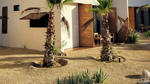 A modern building with a flat roof, large windows, and a gravel courtyard with palm trees and agave plants. - Chic Bungalow with Pool Near the Ocean (El Pescadero)