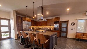 A modern kitchen with a central island, bar stools, and a built-in oven. - Casa Picos Palace with swimming pool and panoramic ocean view in Huatulco Bays (Santa María Huatulco)